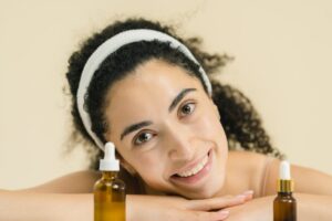 Woman with curly hair smiling, showcasing skincare products, indoors.